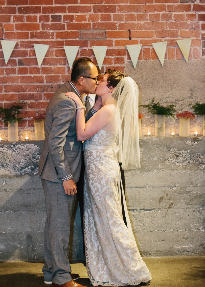 Bride and groom's first kiss at wedding ceremony at Melrose Market Studios in Seattle, WA