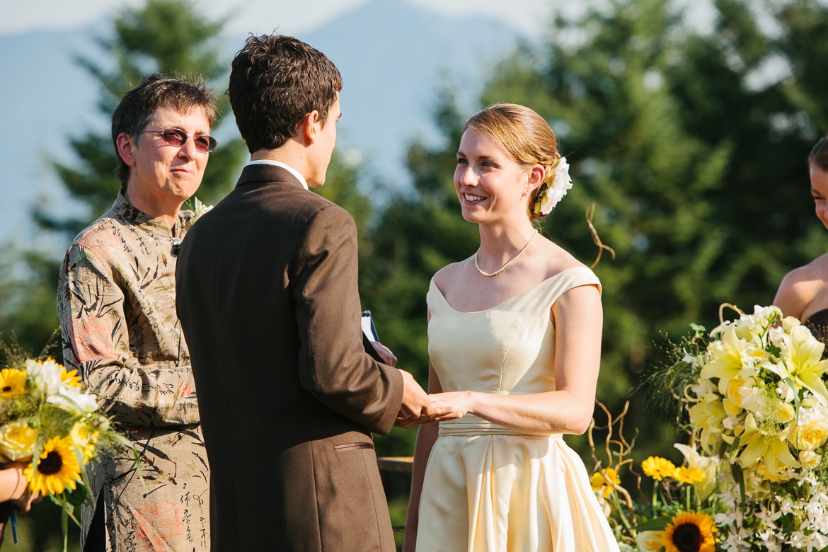 Bride and groom exchanging rings during wedding ceremony at Snoqualmie Point Park with Cascade Mt views