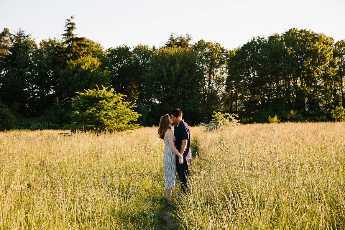 Couple kissing in field during sunset engagement photos at Discovery Park in Seattle, WA