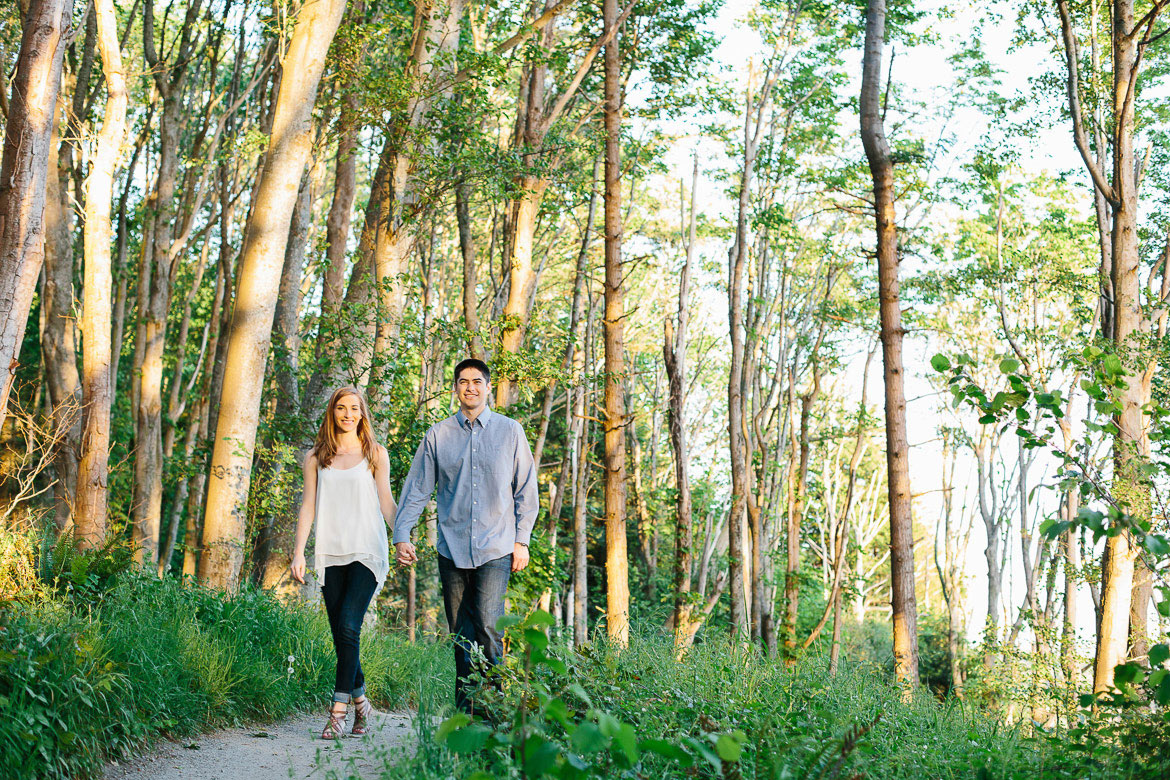 Couple walking down forest trail during sunset engagement photos at Discovery Park in Seattle, WA