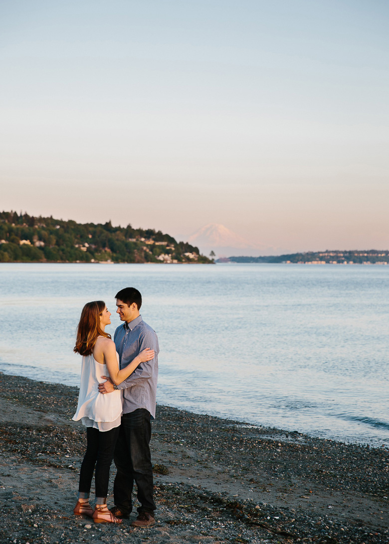 Couple on beach during sunset engagement photos with Mt Rainier in background at Discovery Park in Seattle, WA