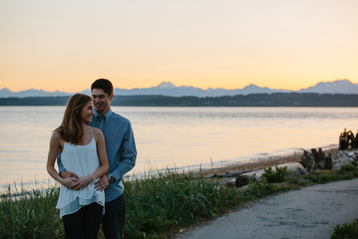 Couple on beach trail during sunset engagement photos with Olympic Mountains in the background at Discovery Park in Seattle, WA