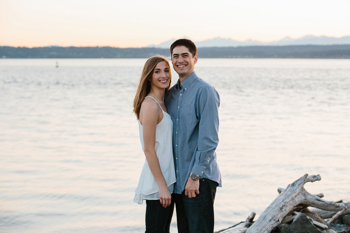 Couple laughing during sunset engagement photos on beach at Discovery Park in Seattle, Washington