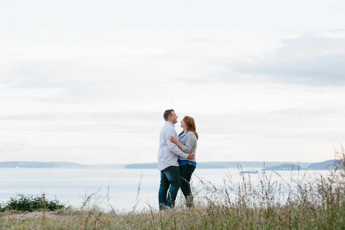 Couple laughing on bluff during sunset engagement photos at Discovery Park in Seattle, WA