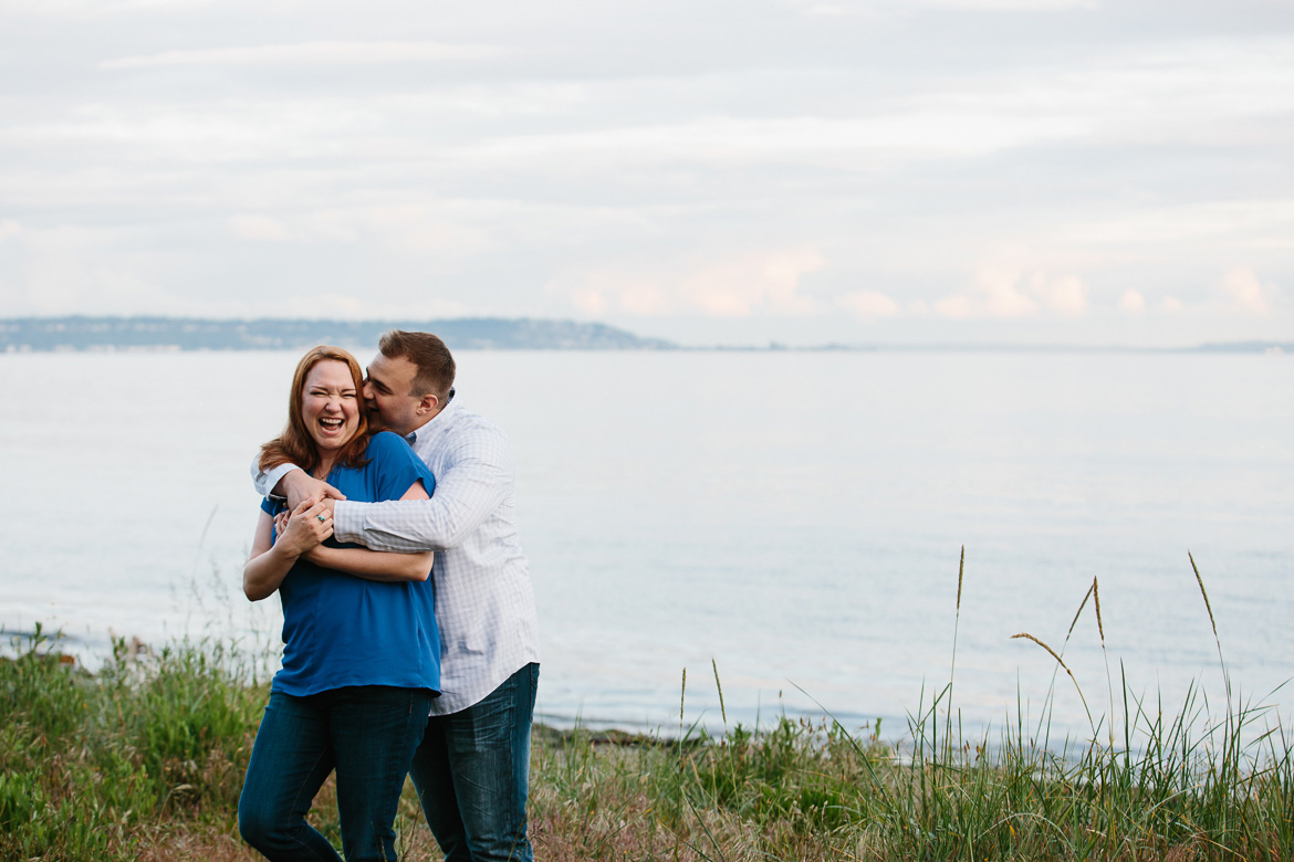 Couple laughing on beach during sunset engagement photos at Discovery Park in Seattle, WA