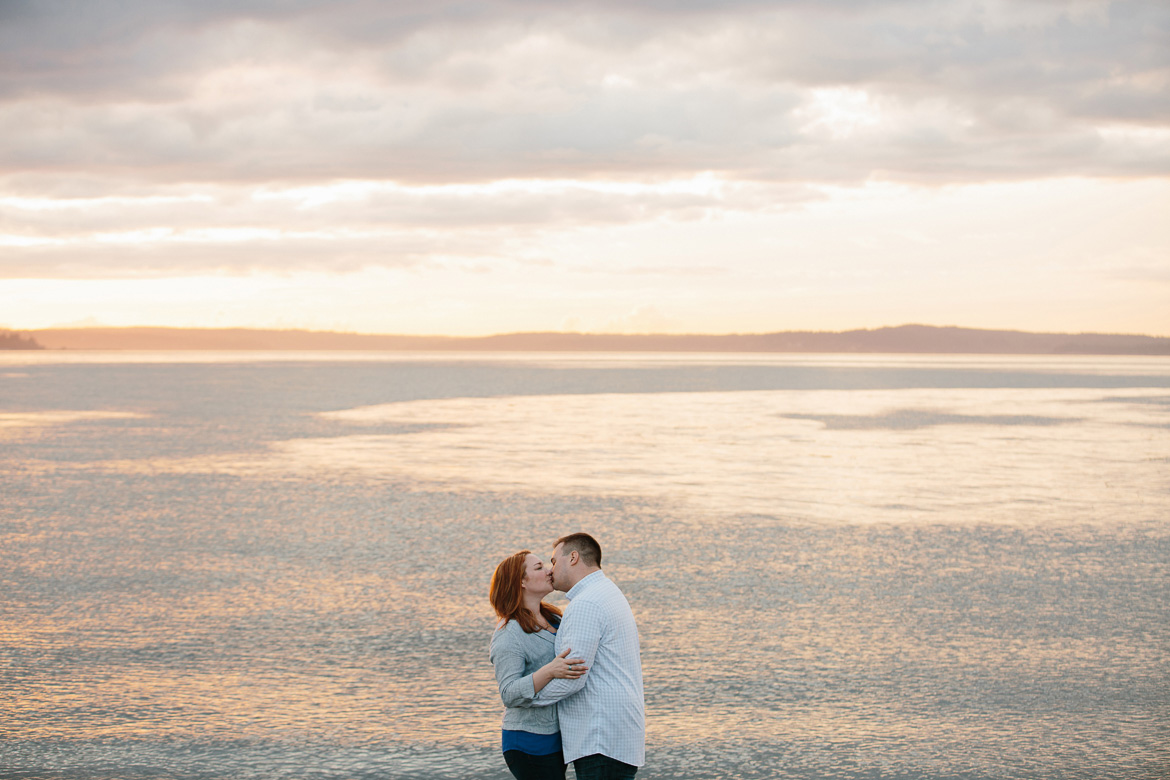 Couple kissing on beach during sunset engagement photos at Discovery Park in Seattle, WA