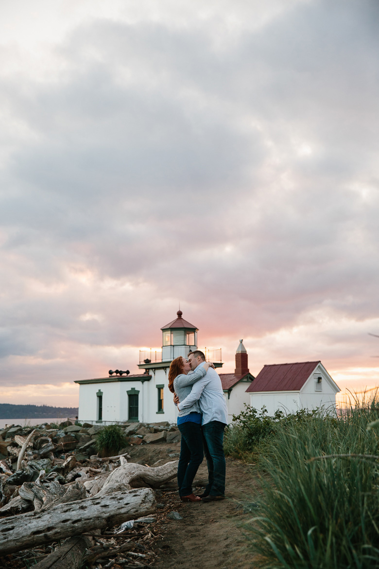 Couple kissing in front of lighthouse during sunset engagement photos at Discovery Park in Seattle, WA