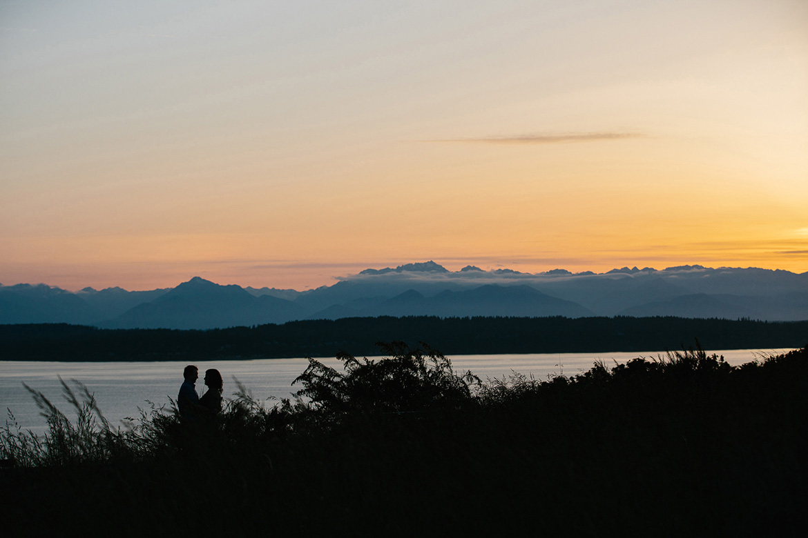 Couple standing on bluff during sunset engagement photos at Discovery Park in Seattle, WA