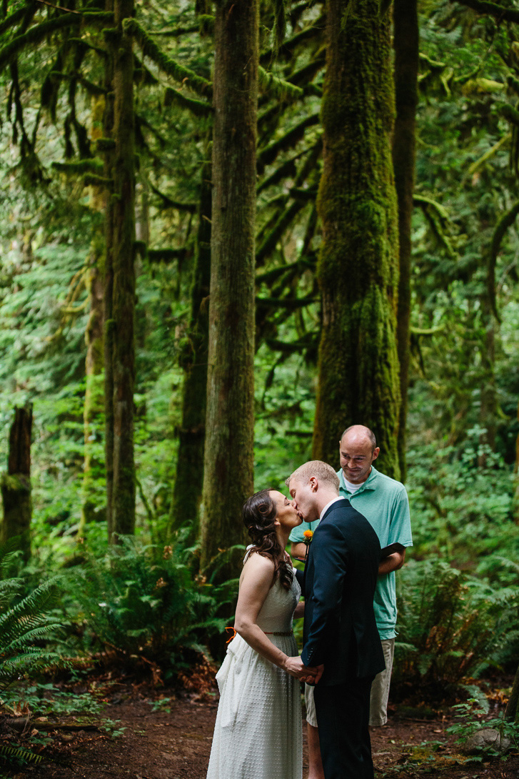 Groom and bride kissing during forest wedding ceremony at Wallace Falls in Gold Bar, WA
