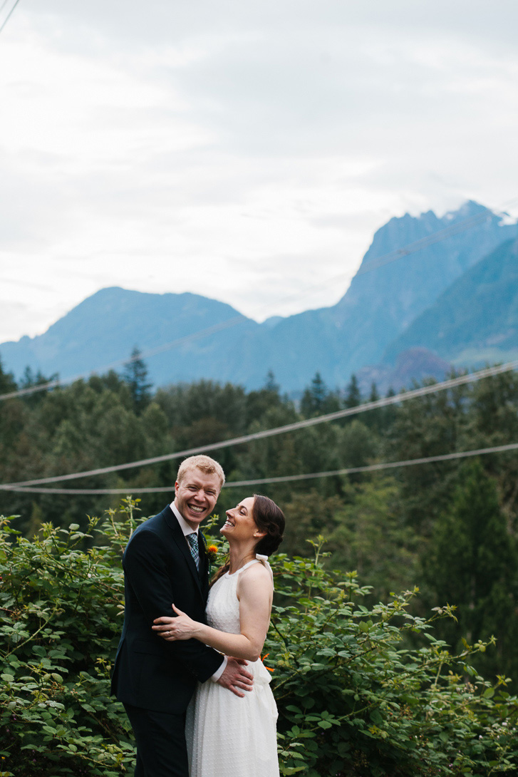 Groom laughing during wedding portraits with view of mountains at Wallace Falls State Park in Gold Bar, WA