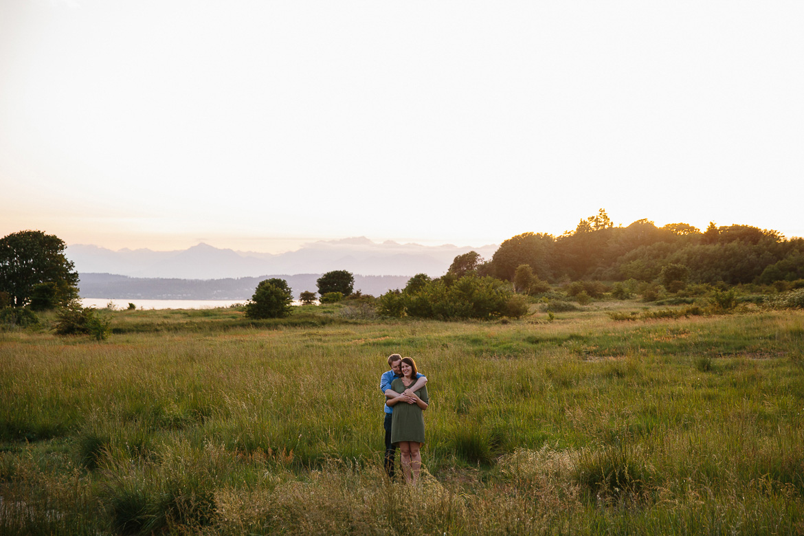 Couple smiling in field during sunset engagement session at Discovery Park in Seattle, WA