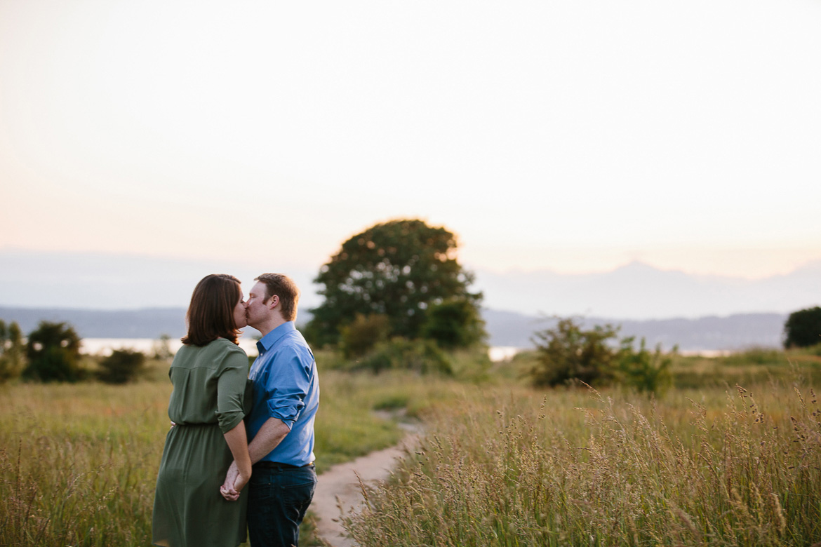 Couple kissing in field during sunset engagement photos at Discovery Park in Seattle, WA