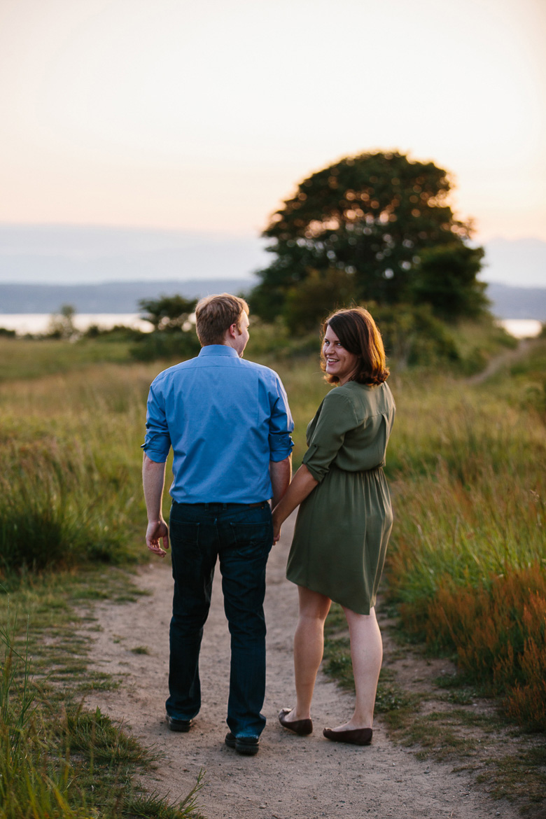 Couple walking and smiling during sunset engagement photos at Discovery Park in Seattle, WA