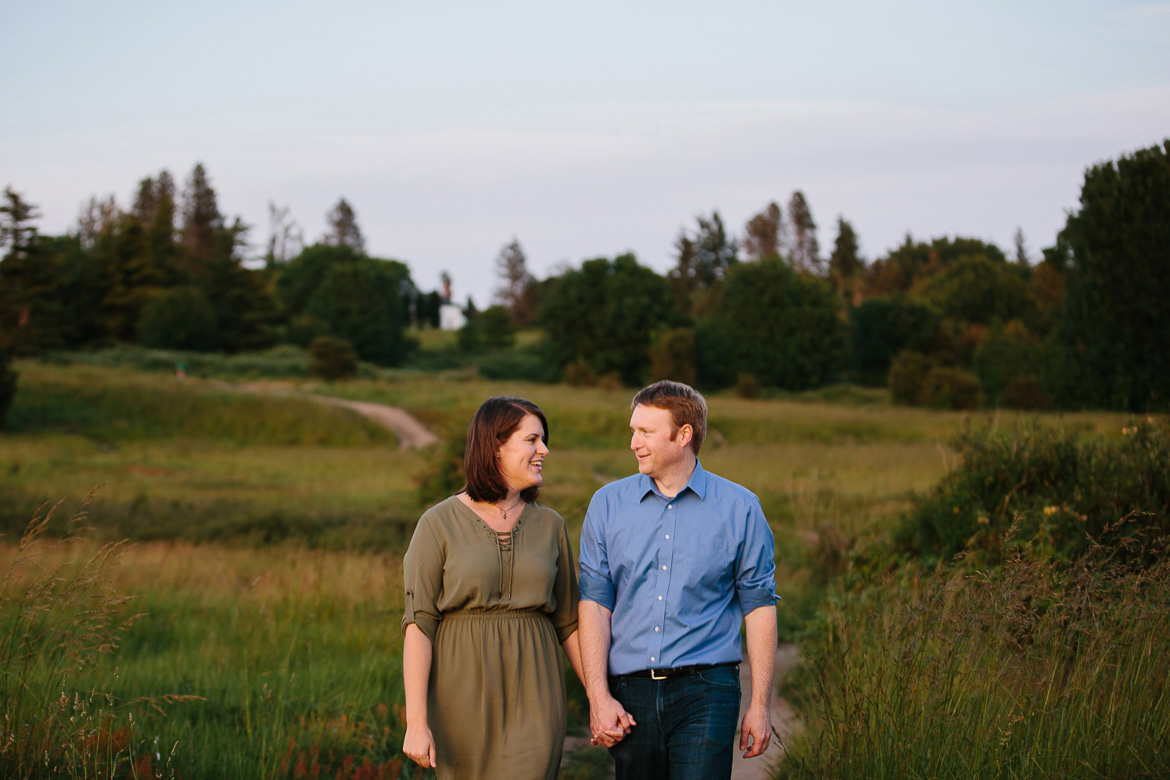 Couple walking in field during sunset engagement photos at Discovery Park in Seattle, WA