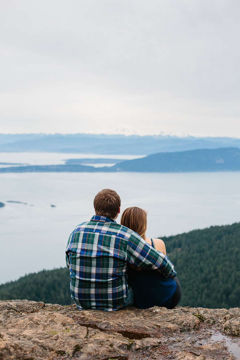 Couple sitting during engagement shoot on Mt Constitution with view of Mt Baker