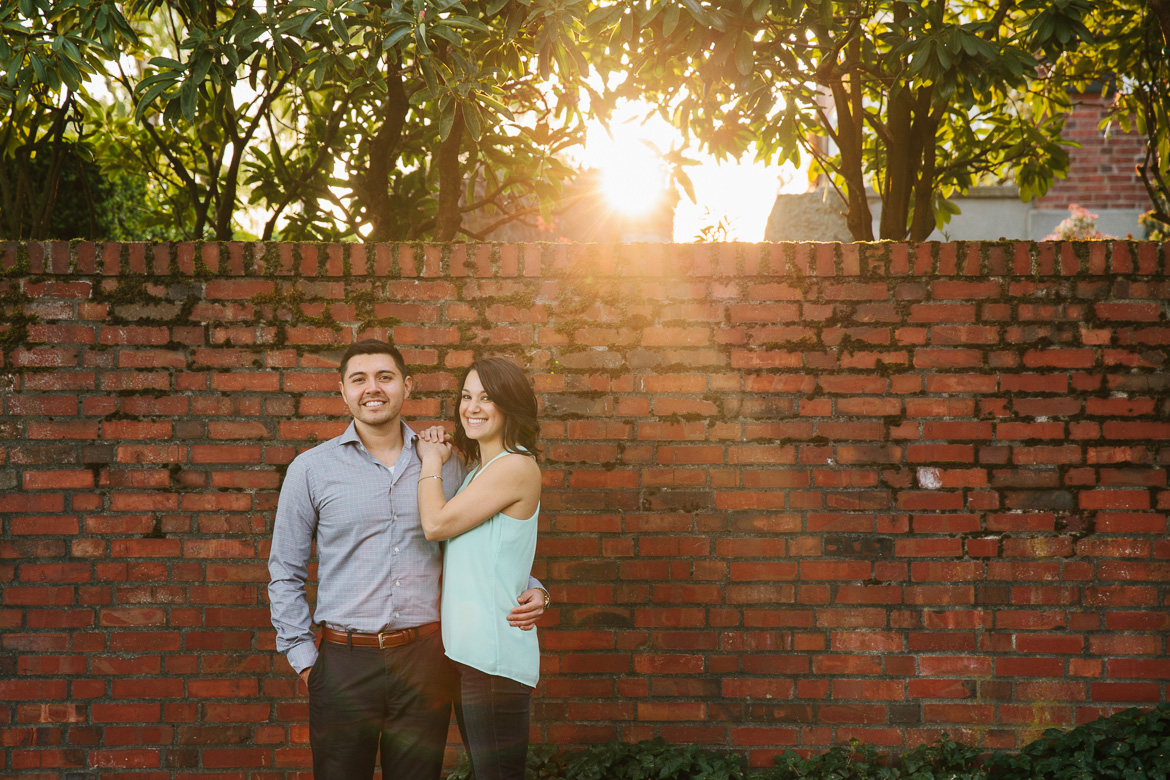 Seattle couple posing in front of brick wall during sunset photo session on Upper Queen Anne